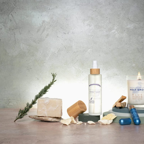 Collection of wellness products including a candle, bottle, and stones on a wooden surface with a concrete wall background.